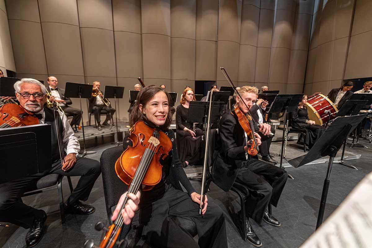 San Juan College Orchestra with violinists smiling while playing