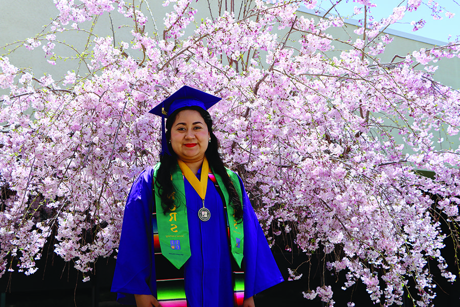 毕业典礼上，身着荣誉流苏的礼服，站在粉红色的花树前