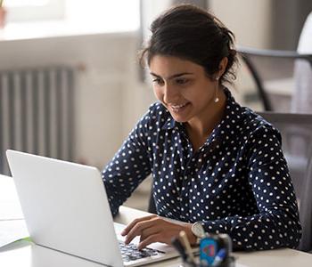 Person, wearing polka-dot blouse looking at laptop.