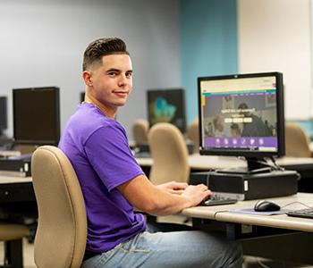 Person wearing purple shirt, sitting a computer.