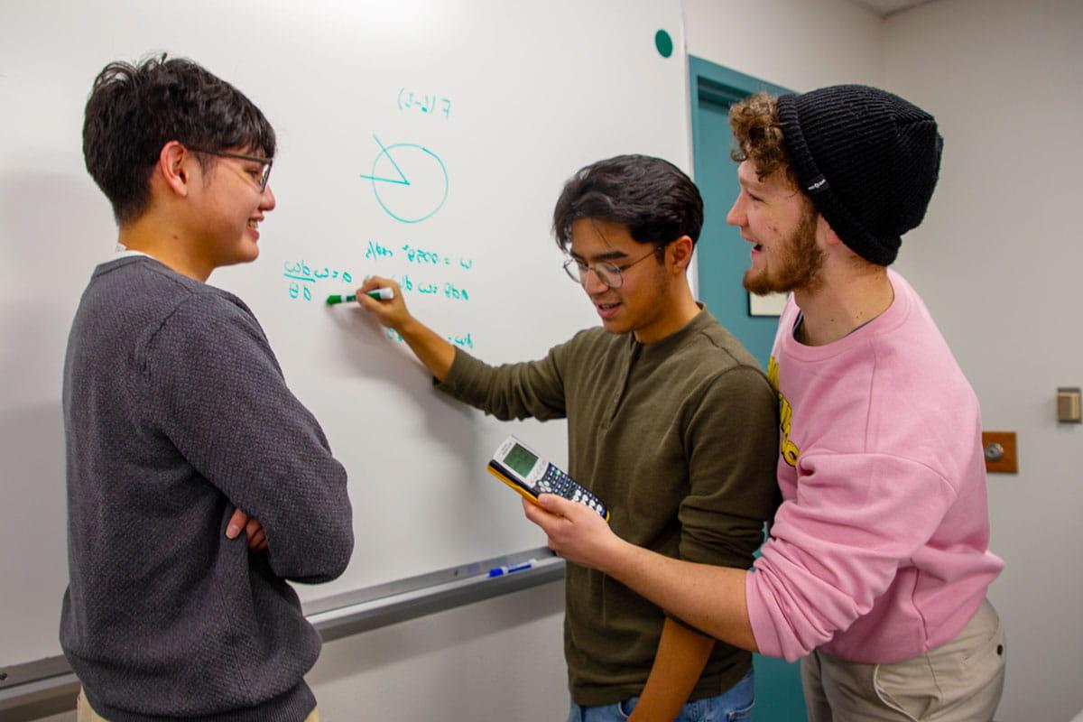 Three 太阳集团娱乐场登陆网站 students working on a math problem on a whiteboard