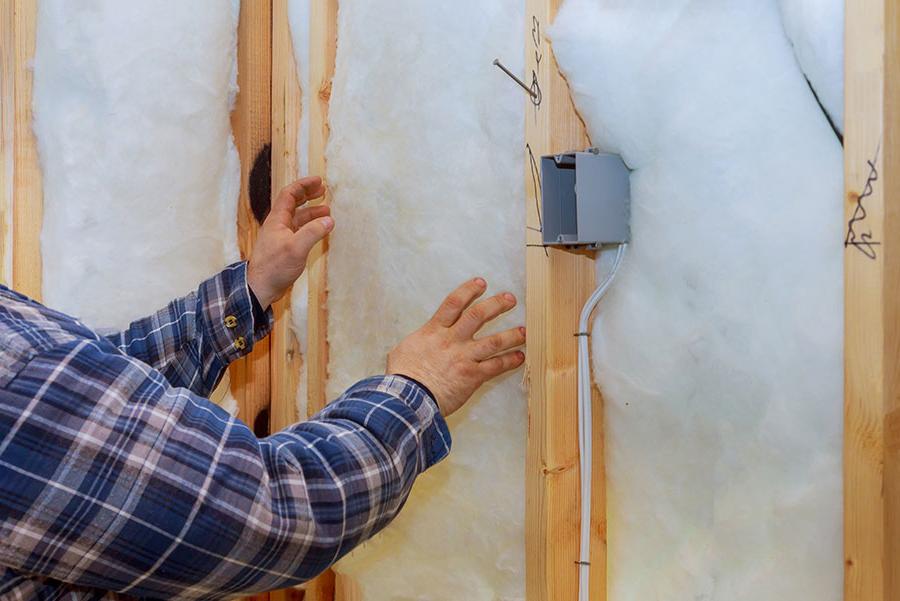 A man installing insulation into a framed wall.