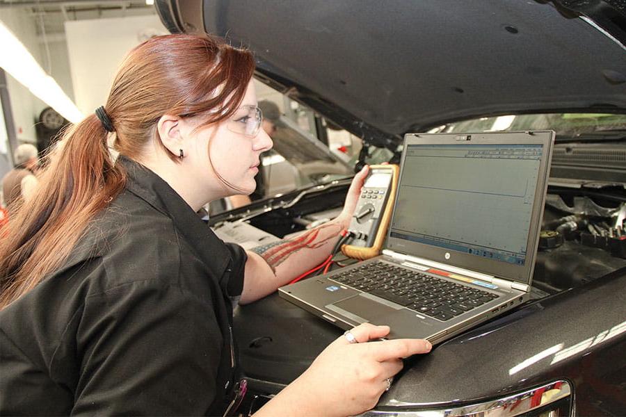 San Juan College student using a diagnostic tool and laptop on a car