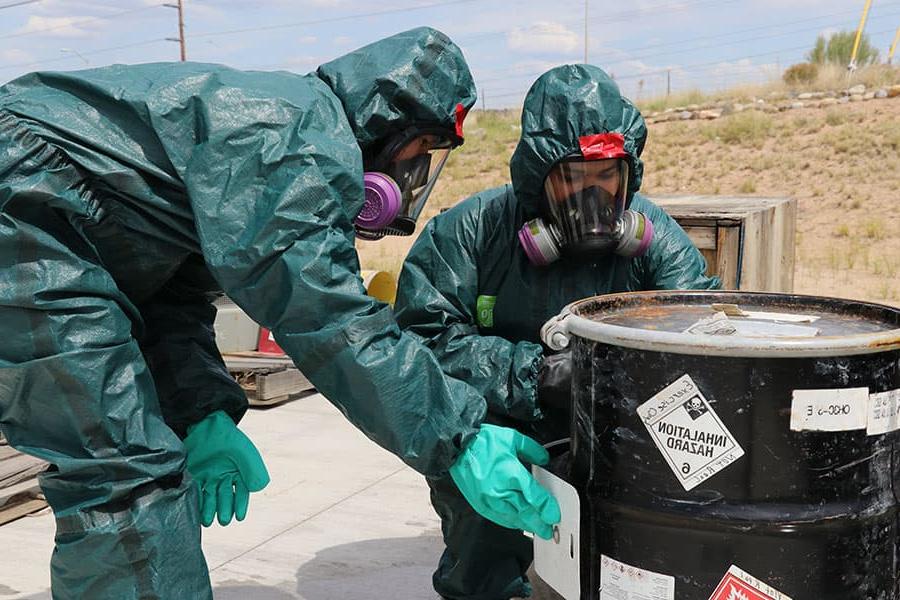两个穿着防护服的人正在检查一个装有危险物质的容器