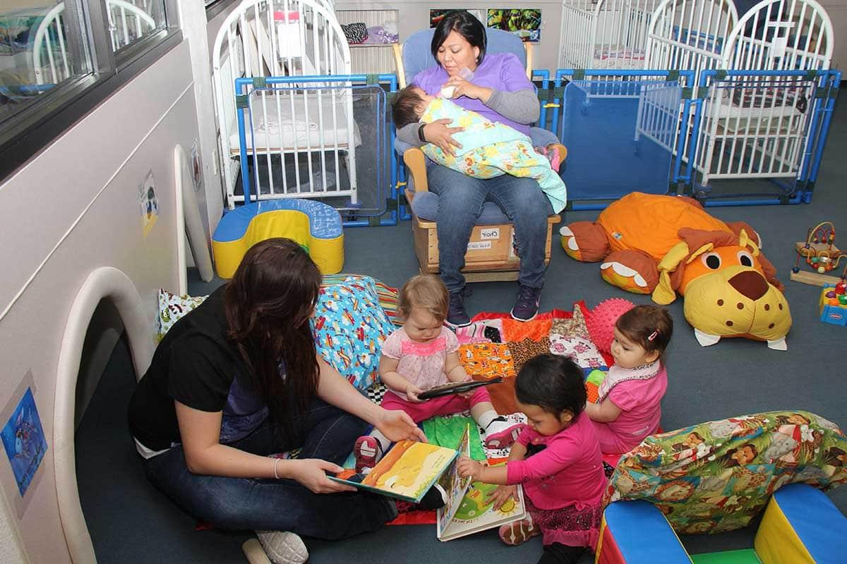 A CFDC teachers reading to three toddlers and one teacher feeding a baby